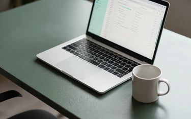 A high-angle photograph of a sleek, dark slate green metal desk with a modern laptop. The screen shows a clean financial dashboard with soft aqua accents. A ceramic mug in mist white sits nearby under soft, professional lighting.