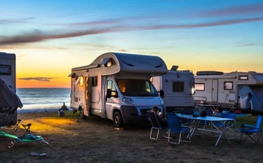 Motorhomes and camper vans parked at a scenic beach campsite during a vibrant coastal sunset.