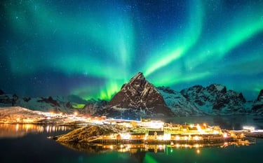 Vibrant green northern lights aurora borealis over a snowy mountain and glowing village in Lofoten, Norway.