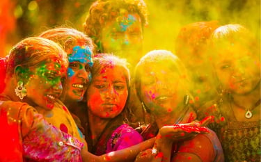 A group of women celebrating the Holi festival with colorful powder and bright yellow light.