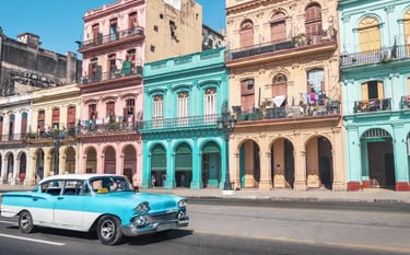 A blue and white classic vintage car drives past colorful colonial buildings in Old Havana, Cuba.