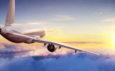 A commercial airplane flying high above white clouds during a vibrant golden sunset.