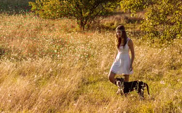 Young girl walking through a field of long grass with a dog
