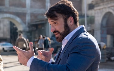 Photo of the side profile of an actor (in a suit) explaining to someone outside the image left side