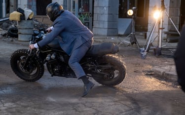 Stuntman on motorbike doing a wheel slide set off in front of main camera moving off left of image 