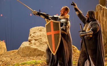 Two extras in medieval knight costumes looking to the left and cheering on a blue screen background 
