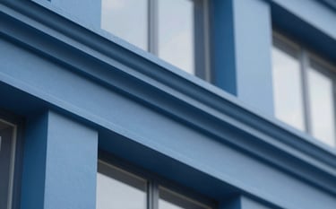 Close-up of a high-quality paint finish on a modern building facade with clean lines and architectural detail. Professional blue tones #4C7B9E are visible in the structural elements. Bright, clear daylight highlighting the professional quality of the exterior finish.