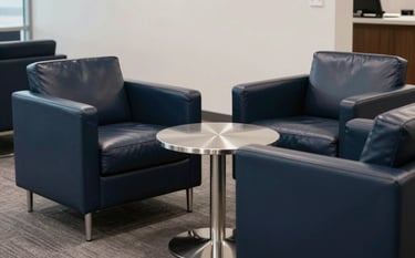 A clean and modern North American corporate lounge area with deep navy leather armchairs and a polished steel table. The lighting is soft and professional, emphasizing a discreet and supportive business environment without showing people.