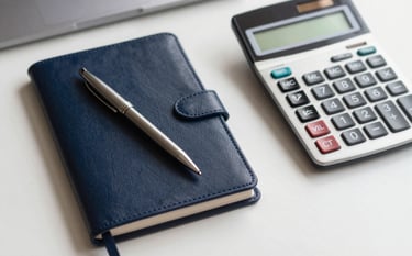 A close-up, top-down shot of a tidy Indian corporate workspace. A high-quality pen rests on a leather-bound notebook next to a modern calculator. The scene is illuminated by soft, natural morning light, featuring a palette of Dark Navy and Off-white. Authoritative and sophisticated.