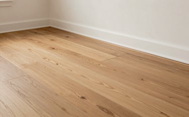 Detailed photography of high-quality hardwood flooring being installed in a minimalist North American home. The image features clean lines, off-white walls, and a professional finish, highlighting the reliable craftsmanship of Ontario-based renovation experts.
