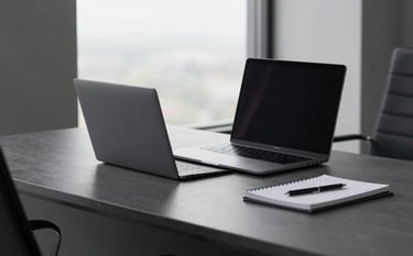 A high-end, minimalist North American / International corporate office setting. A sleek charcoal grey desk holds a slim laptop and a notebook. Soft daylight enters from a large window. The aesthetic is clean and professional, featuring a palette of charcoal and steel grey.