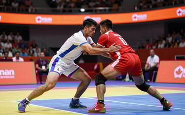 High-intensity Kabaddi league match action. A raider in a white jersey with blue accents attempts to touch a defender. The background shows a modern arena with vibrant orange highlights. The mood is competitive and electric, featuring professional Canadian sports aesthetics.