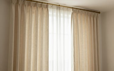 A high-end living room featuring floor-to-ceiling custom linen drapes in a soft cream color. The drapes are perfectly pleated and hang from a minimalist bronze rod. The lighting is warm and airy, casting soft shadows. The color palette includes #F9F7F3 and subtle #7A5B44 accents in the hardware.
