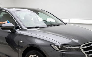 A clean, modern North American US detailing bay with a polished dark sedan. A professional is applying a high-gloss finish. Bright, informative atmosphere with silver and off-white accents, crisp reflection on paint.