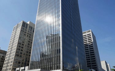 Wide shot of a modern glass skyscraper in a South American business district like Avenida Paulista, bright blue sky reflecting on the windows, clean and professional atmosphere.