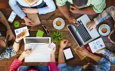 a group of people sitting around a table with laptops