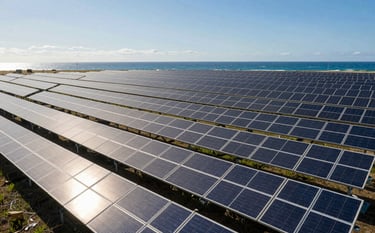 Wide-angle photograph of a massive solar farm with rows of high-tech photovoltaic panels under a bright ocean blue sky. The composition is clean and modern, emphasizing sustainable energy and innovation with soft off-white reflections on the glass surfaces.