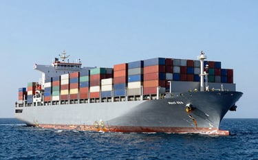 A large commercial shipping vessel carrying multi-colored containers through deep ocean blue waters. The lighting is bright and clear, showcasing the power of global trade and logistics. Sophisticated architectural style photography.