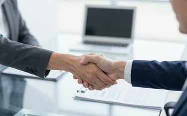 A high-angle shot of a glass table with two professionals shaking hands in a bright, minimalist boardroom. The lighting is clean and professional, emphasizing the efficiency and reliability of Soluc Financas LTDA.