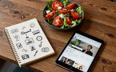 A top-down view of a professional content planner's desk in a modern North American / Western cafe, featuring a notepad with handwritten marketing ideas, a tablet showing a social media feed, and a fresh tomato salad, captured in a cozy Scandinavian style with warm natural light and accents of deep ripe crimson and matte forest green.