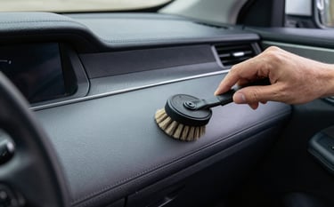 Detailed interior shot of a clean modern vehicle cabin in a North American setting. A professional detailer is using a soft brush to clean the dashboard seams. The leather looks supple and the slate grey and dark navy textures are pristine.