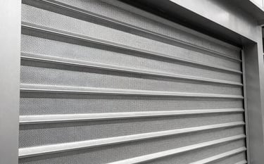 A close-up photograph of a professional 3D illuminated sign mounted on a modern dark slate building facade. The lighting is soft off-white, highlighting the metallic precision and high-quality finish of the logo.