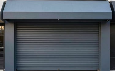 Architectural shot of a storefront featuring a robust charcoal grey rolling metal curtain and a stylish muted slate blue awning. The composition is clean, showcasing industrial durability.