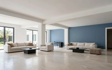 Wide shot of a beautifully renovated open-space living area in a Southern European villa. High ceilings, pristine white and slate blue walls, and polished flooring. The furniture is minimalist and elegant, reflecting a blend of technical precision and refined Italian design. Bright, airy, and professional atmosphere.