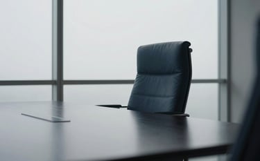 A professional photograph of a minimalist boardroom. A sleek black table occupies the center, reflecting a soft mist white light from a large window. The atmosphere is quiet and intelligent. One leather chair in deep midnight blue is slightly pulled out, suggesting an exclusive meeting about to take place.