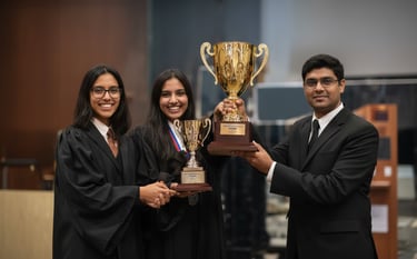 Photograph of three students in dark suits holding a large golden trophy.