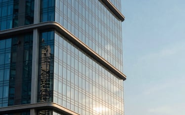 An architectural photograph of a luxury property in Dubai showing a sleek glass facade reflecting the morning sun. The composition focuses on clean lines and sophisticated modern design. Deep blue and light cyan sky tones dominate the background. Middle Eastern / Gulf architecture.