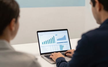 An over-the-shoulder photograph of an entrepreneur working on a laptop at a contemporary desk in a North American tech hub. The screen displays professional financial projections. The background is a clean, off-white office wall with light blue accents. Strategic and focused mood.