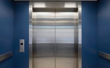 A sleek, modern elevator interior with brushed steel doors in a professional East African / Mozambican office building. The lighting is crisp and clean, reflecting a trustworthy and innovative engineering brand. Colors include midnight blue and pale mist gray.