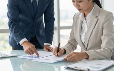 A high-end professional office setting in Brazil. Two colleagues in business attire are reviewing structured documents on a clean glass desk. The atmosphere is bright with natural light from large windows. The scene reflects total organization and strategic planning. Colors include slate blue and off-white.