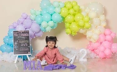 a baby girl sitting on a table with balloons and balloons