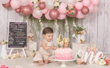 a baby girl in a pink dress and a pink cake