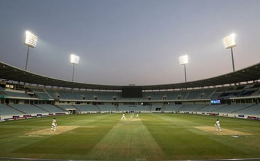 A high-end, wide-angle photograph of a modern cricket stadium in India at dusk, illuminated by powerful white and gold floodlights, creating a premium and professional atmosphere.