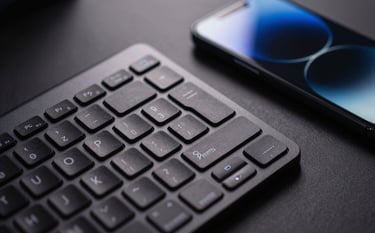 Close-up of a high-end keyboard and a sleek smartphone in a modern North American / US workspace. The lighting is dramatic and professional, using deep charcoal and vibrant azure lighting highlights.