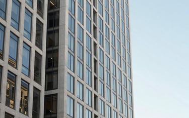 Architectural photography of a contemporary financial district in the North American West Coast. A sharp focus on a glass and steel building reflecting a clear morning sky. The image uses a clean palette of off-white and light blue, conveying stability.