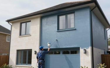 The exterior of a contemporary Shrewsbury home with clean masonry. A professional spray painting system is being used to apply a smooth coating in a sophisticated #4E7D96 slate blue. The image conveys precision, efficiency, and professional quality with crisp outdoor lighting.