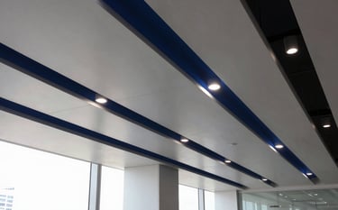 A high-end modern office interior in a South American / Brazilian city, featuring a sophisticated suspended ceiling design with integrated LED lighting. The style is minimalist with steel blue accents. The photography captures the clean lines and the precision of the installation, conveying professional innovation.