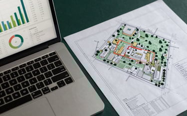 Professional high-angle shot of a desk with a laptop displaying analytical charts and a set of architectural site plans for a major civil works project. Palette includes deep forest green and muted pine. Sharp focus on the precision of the work, Australian / International context.