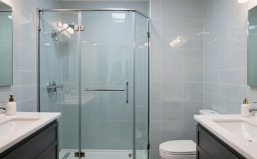 A contemporary bathroom renovation in a North American / Canadian (with South Asian cultural influence) residential setting. Features include soft light blue tiling, a sleek glass walk-in shower, and a minimalist vanity. The lighting is bright and clean, reflecting modern craftsmanship.