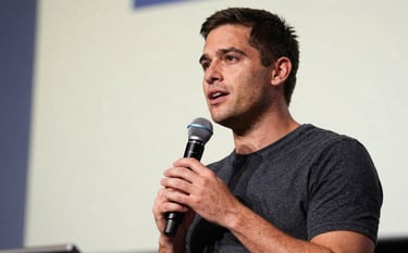 Close-up of a motivational speaker holding a microphone on a stage in a North American / US conference hall. Background is a soft alabaster with hints of slate blue, capturing a moment of powerful oratory leadership.
