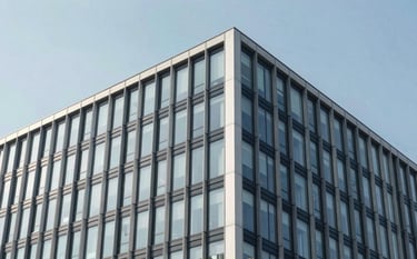A crisp architectural photograph of a modern steel and glass building facade against a sky blue sky. Mist white and midnight navy architectural details are visible.