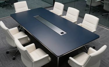 A high-angle photograph of a sleek, modern corporate boardroom. A large midnight navy table is surrounded by mist white chairs. The lighting is bright and professional, emphasizing clean glass lines and authority.