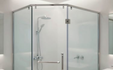 A close-up of a high-end minimalist bathroom featuring a frameless tempered glass shower enclosure. The scene is bright and clean, with soft lighting reflecting off the polished glass and silver fixtures. Incorporates brand colors #F7F9FB and #BCC9D4 for a sophisticated, modern feel.
