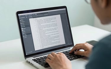 A close-up of a laptop screen showing a detailed manuscript being edited with track changes. A professional Southeast Asian / Indonesian academic is seen from the side, focused on the work in a clean, minimalist home office. Colors: Steel Blue and Soft Mint White.
