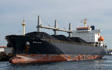 A high-end, professional photograph of a large cargo vessel at a North American industrial port, being loaded with iron ore. The scene features deep slate and muted blue tones of the water and sky, with a sharp focus on the metallic textures of the ship, conveying stability and industrial strength.