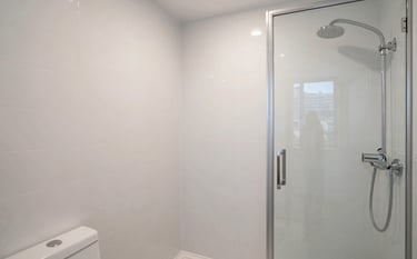 Wide shot of a modern bathroom with newly refinished white wall tiles and a gleaming shower stall in a Manhattan residence. The lighting is crisp and clear, emphasizing a spotless and minimalist look. Professional architectural photography.